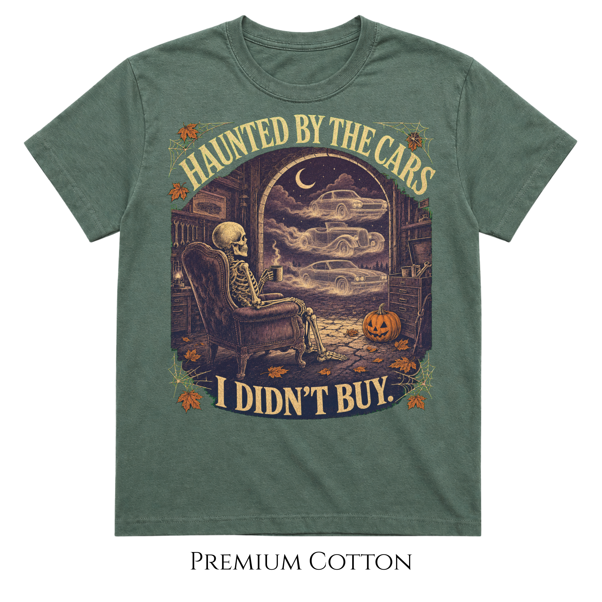 A heathered sage green short-sleeve t-shirt with a vintage Halloween graphic of a skeleton sitting in an armchair and looking out a window at classic cars driving away. The text 'HAUNTED BY THE CARS' is above the graphic, and 'I DIDN'T BUY.