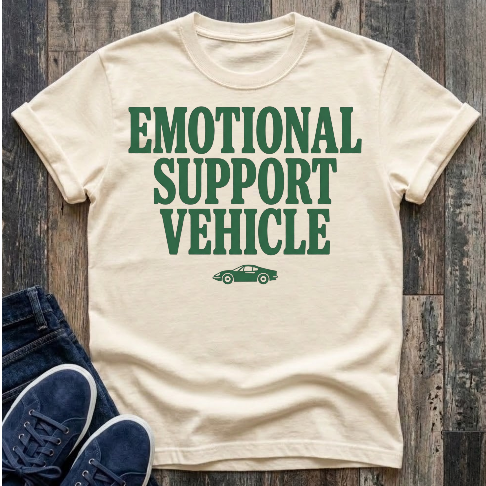 Ivory t-shirt with bold forest green block typography reading "Emotional Support Vehicle" with a small classic sports car silhouette centered beneath the text