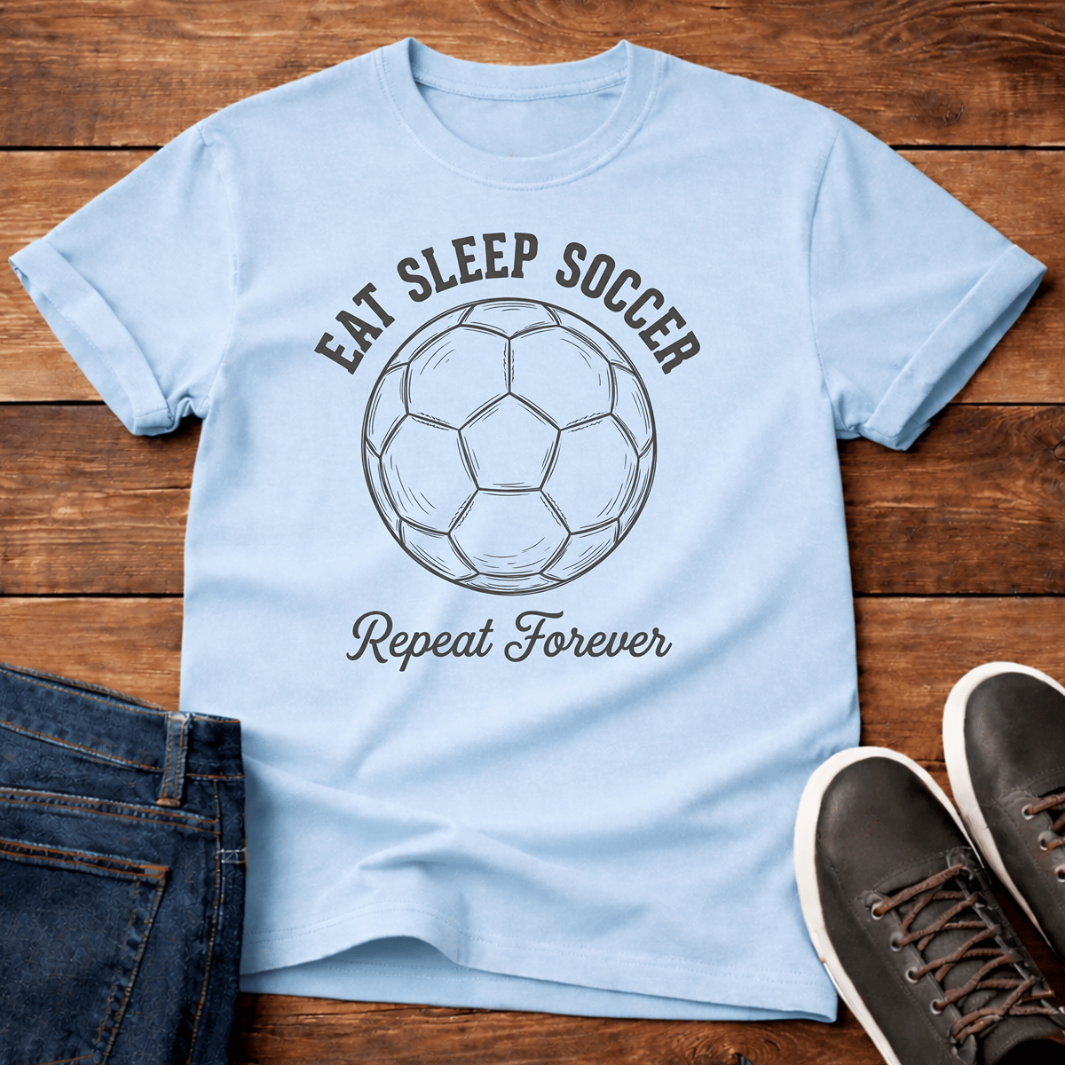 Eat Sleep Soccer Repeat T-Shirt in light blue with a soccer ball graphic and bold text.