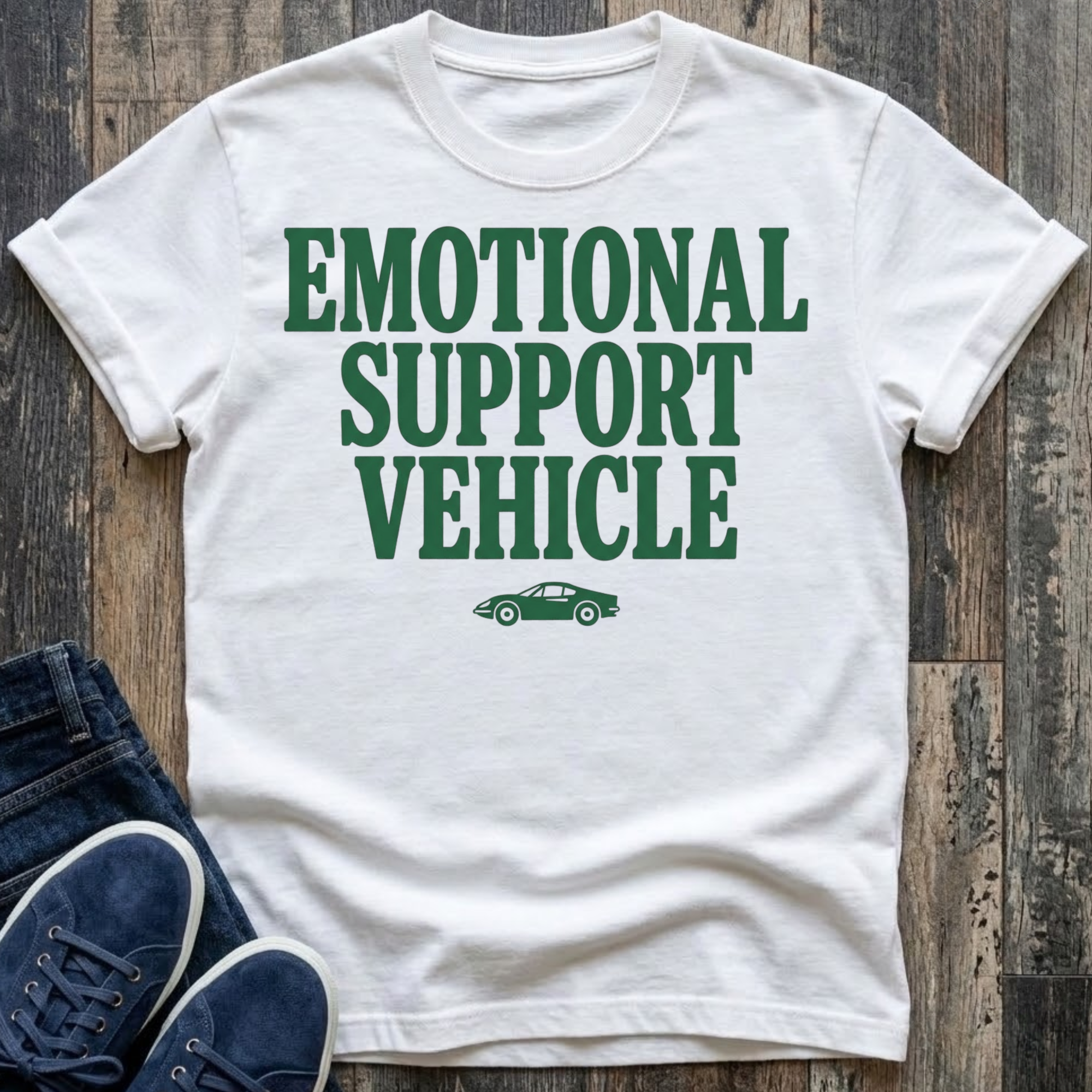 White t-shirt with bold forest green block typography reading "Emotional Support Vehicle" with a small classic sports car silhouette centered beneath the text