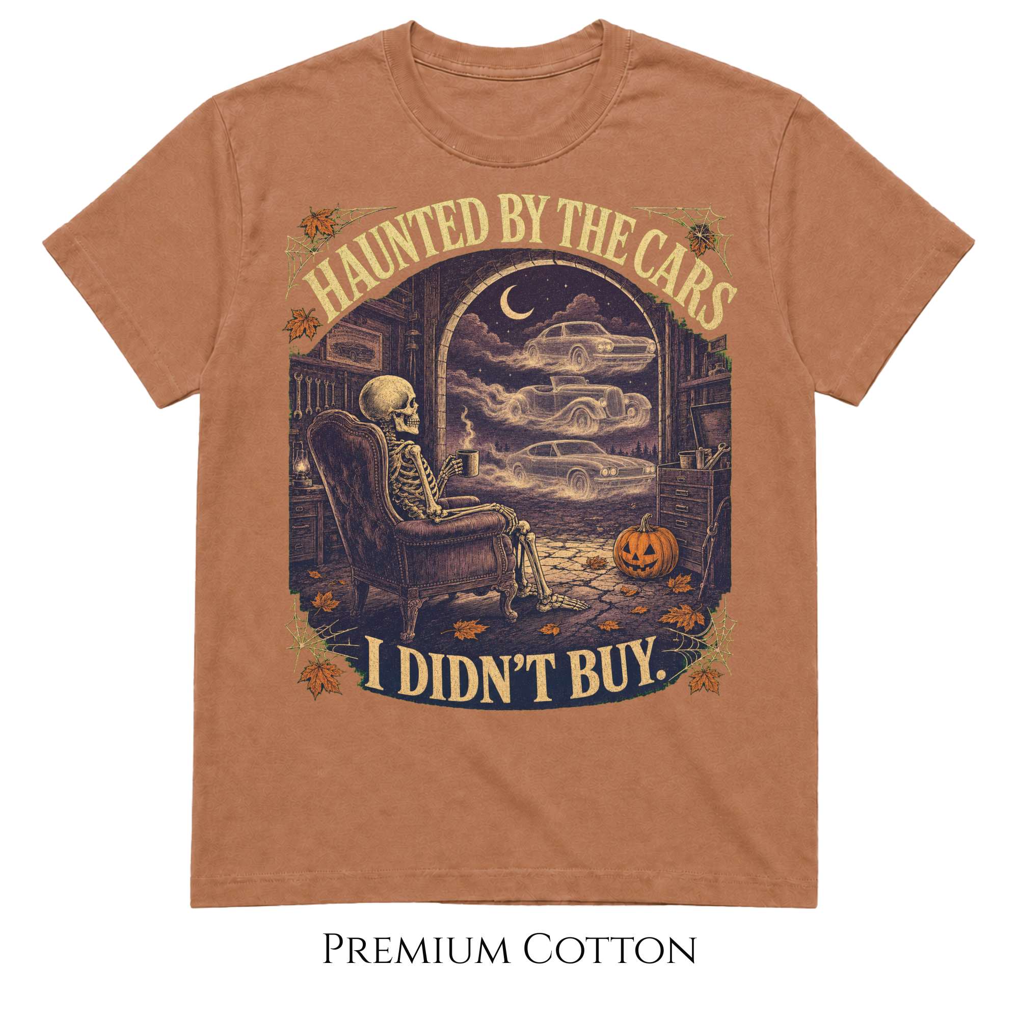 A rust-brown short-sleeve t-shirt with a vintage Halloween graphic of a skeleton sitting in an armchair and cars driving through a foggy night scene, with the text 'HAUNTED BY THE CARS I DIDN'T BUY.' Below the shirt, the text 'PREMIUM COTTON' is printed on a white background.