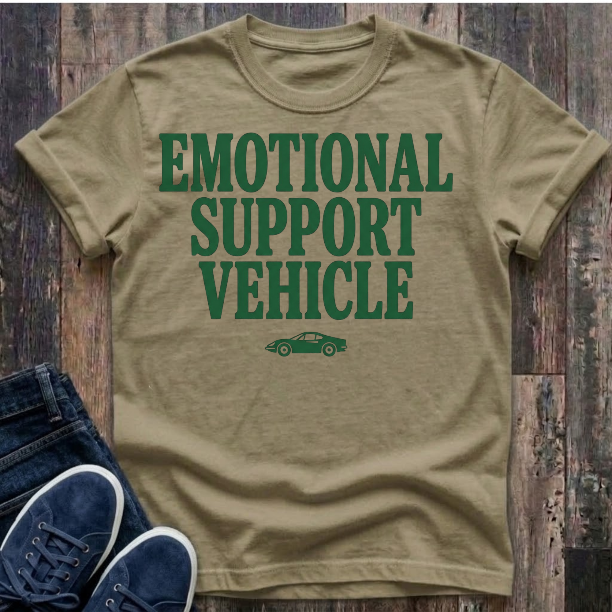 khaki t-shirt with bold forest green block typography reading "Emotional Support Vehicle" with a small classic sports car silhouette centered beneath the text