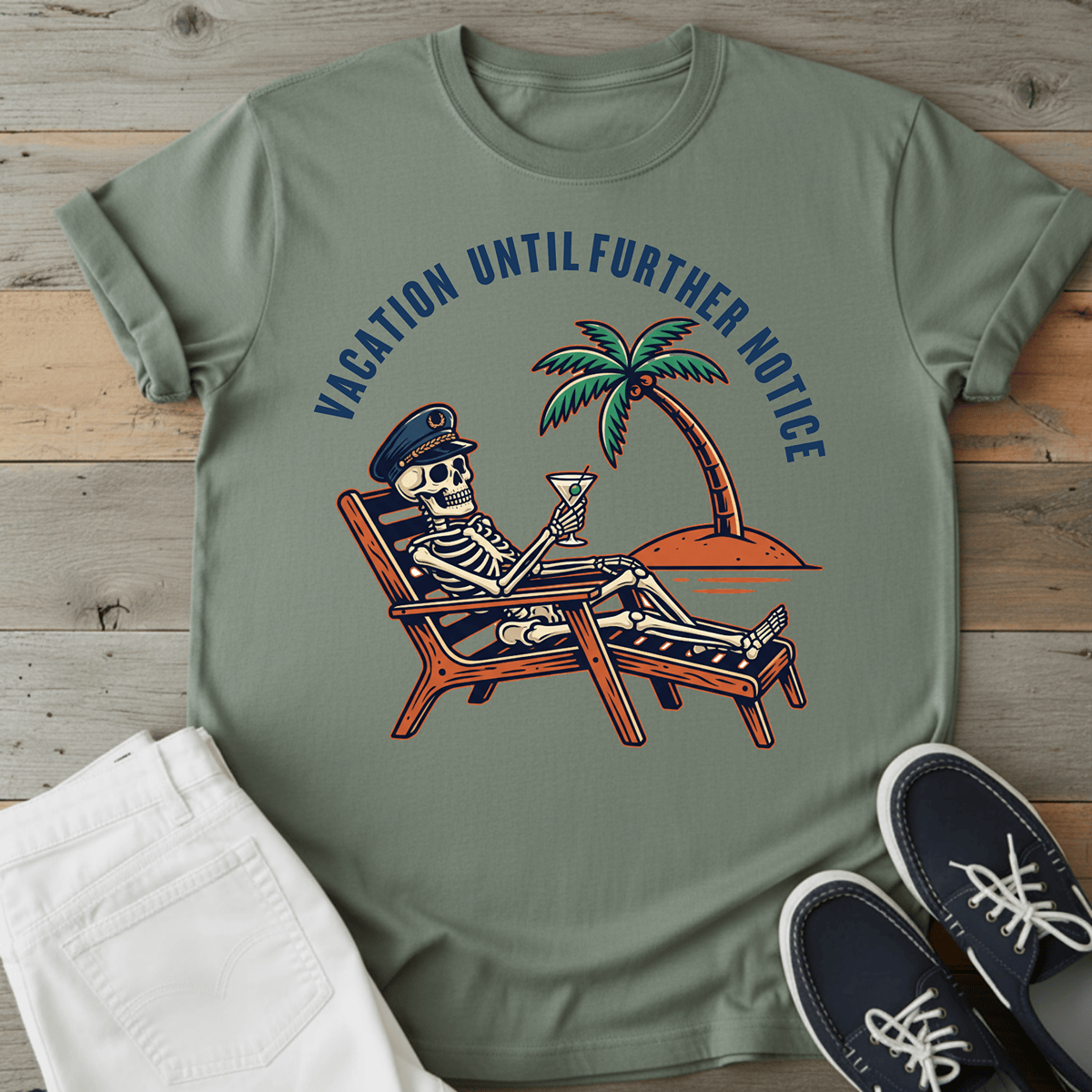 Optimistic Castaway T-Shirt featuring a skeleton relaxing with a drink under a palm tree, in a muted green color.